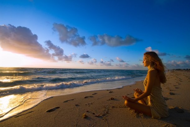 belle-femme-medite-sur-la-plage-sur-le-sable-bord-de-l-eau-face-au-soleil